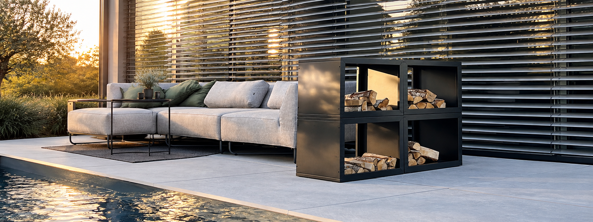 Modulares Feuerholzregal Vancouver aus Edelstahl mit gestapeltem Kaminholz, auf sonniger Terrasse neben Loungesofa und Pool, im Hintergrund Lamellenfassade im Abendlicht