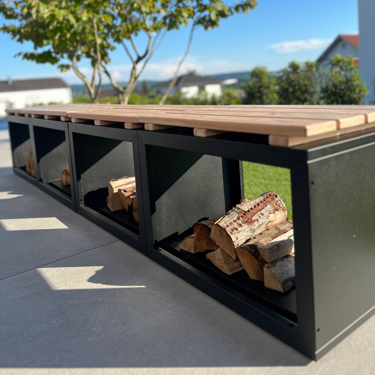 Feuerholzregal Vancouver mit Holzauflage als Sitzbank im Garten, mit Kaminholz bestückt