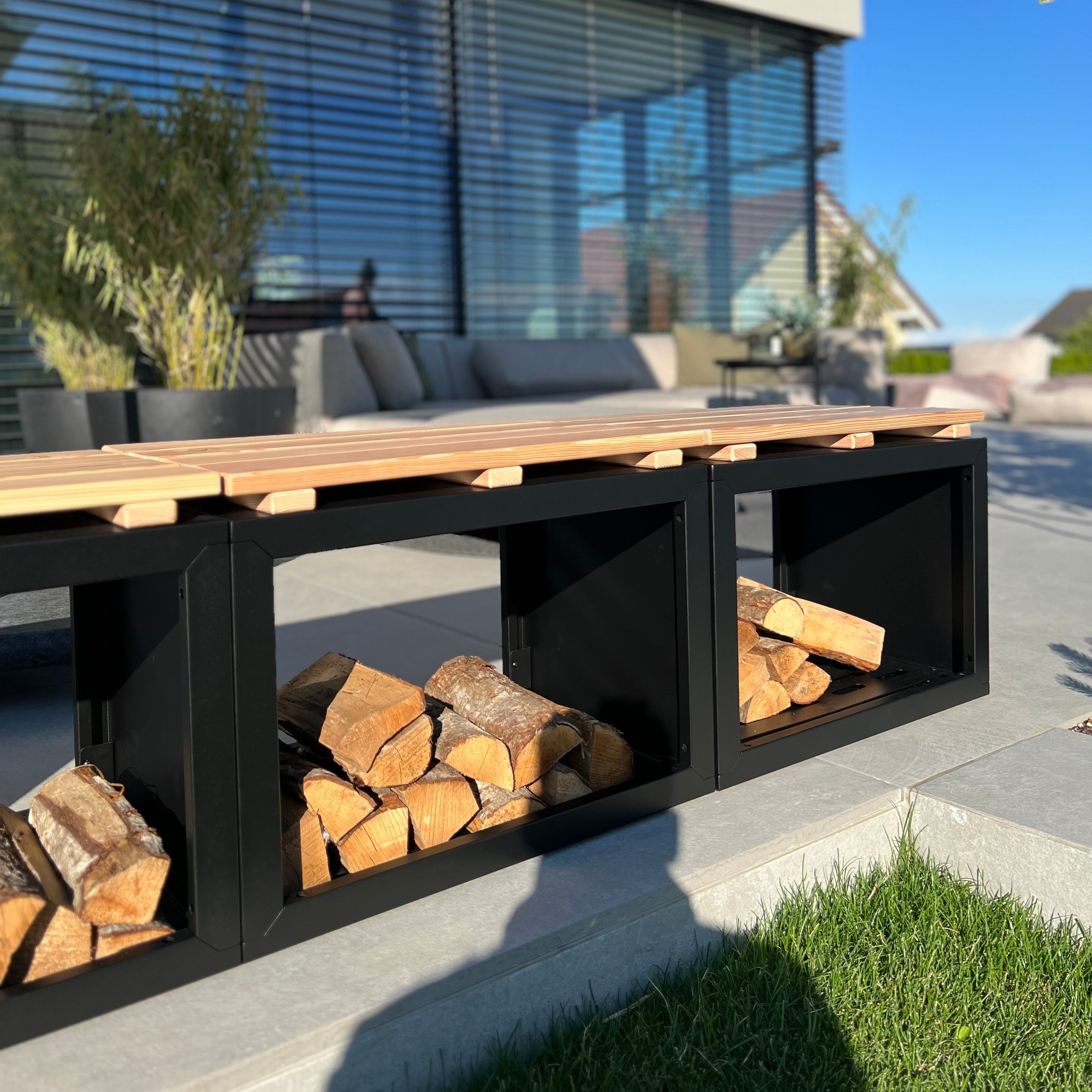 Feuerholzregal Vancouver mit Holzauflage als lange Sitzbank im Garten, mit Kaminholz bestückt
